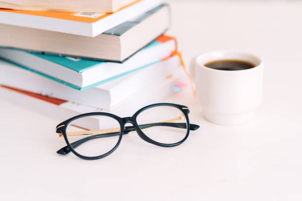 istock Stack of books with glasses and cup of coffee standing on white table 1390857069