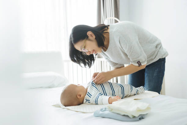 istock Asian mother playing with baby boy while dressing him on bed 1390857128
