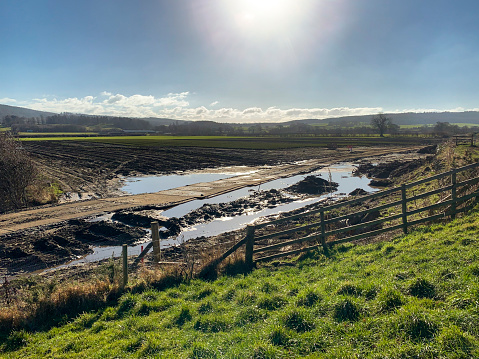 A flooded field in Northumberland, England. There is a road running through the field and has been eroded from the rainfall. The sun is shining above the field.