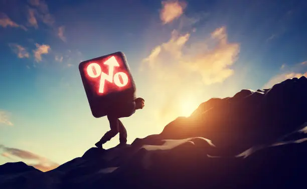 Photo of Man carrying heavy stone with growing interest rate symbol