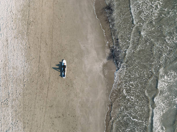 Aerial view of a man lying down on his surfboard on the beach. His relaxing himself before surfing.