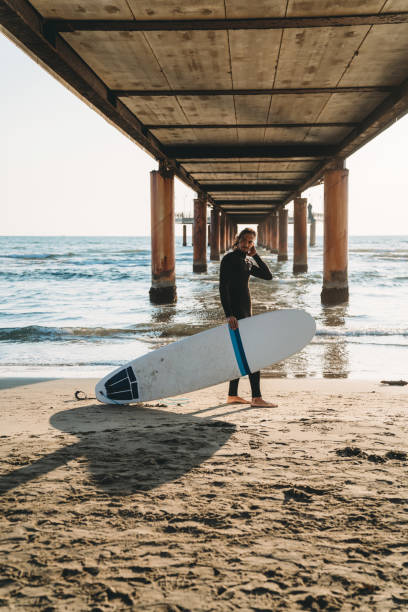 istock A man is standing on the beach under a pier with his surfboard 1390861688