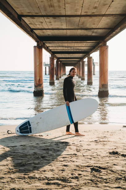 istock A man is standing on the beach under a pier with his surfboard 1390861689