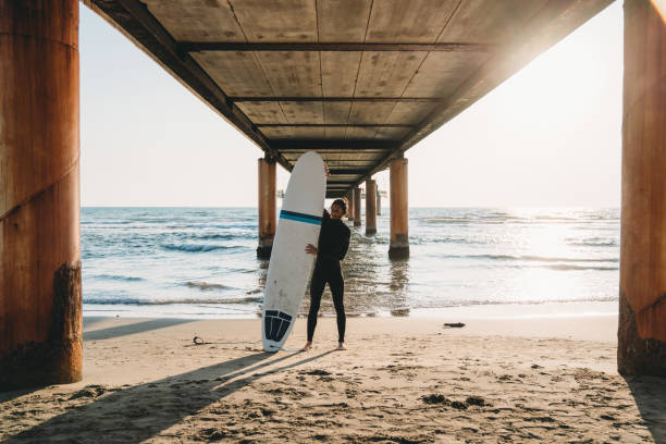 istock A man is standing on the beach under a pier with his surfboard 1390861691