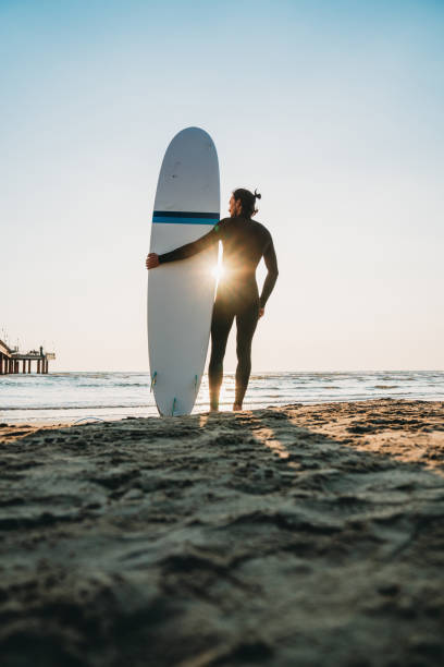 istock A man is standing on the beach with his surfboard, admiring the sunset 1390861703
