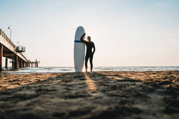 istock A man is standing on the beach with his surfboard, admiring the sunset 1390861705