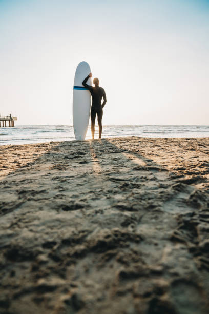 istock A man is standing on the beach with his surfboard, admiring the sunset 1390861715