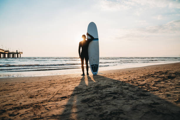 istock A man is standing on the beach with his surfboard, admiring the sunset 1390861724