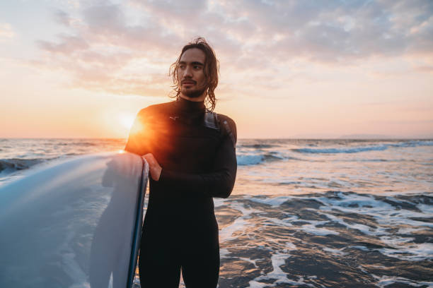A surfer with his surfboard in the sea at sunset. He's wearing a wetsuit.