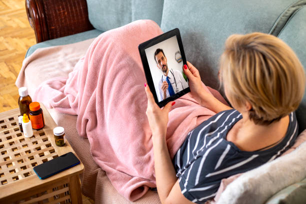 Telemedicine Mature woman using digital tablet  for conversation with her doctor. She is  lying on the couch in the living room and has video call and consultation  with her doctor. virtual event stock pictures, royalty-free photos & images
