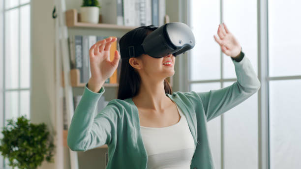 istock Young Asian woman feeling excited while using 360 VR headset for virtual reality, metaverse at home 1390868008
