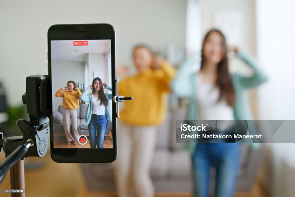 Asian young woman with her friend tiktoker created her dancing video by smartphone camera together. To share video to social media application Dancing Stock Photo
