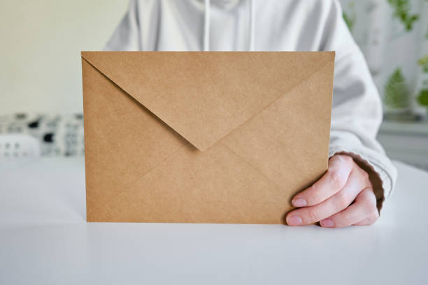 istock Envelope in hands on a light background. New mail, message. Postal service. The person wants to send or receive a letter. Empty envelope, empty space. The concept of people communication. Mockup 1390876169