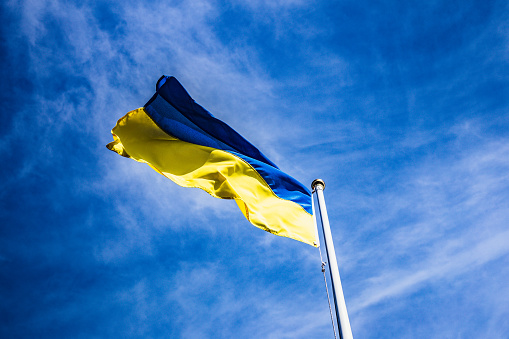 Color image depicting the national flag of Ukraine raised on flagpoles and proudly flying in the wind against a clear blue sky.