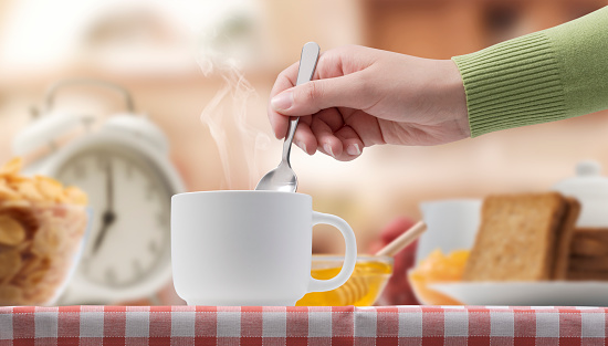 Woman having a delicious breakfast at home, she is stirring tea