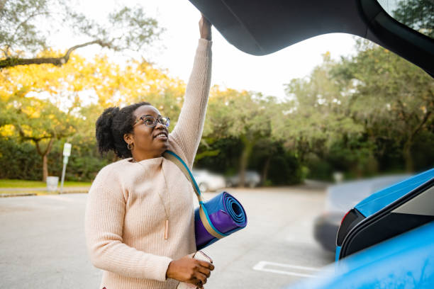 African American Woman in 40s with a Yoga Mat Closing Car Trunk in a Parking Lot