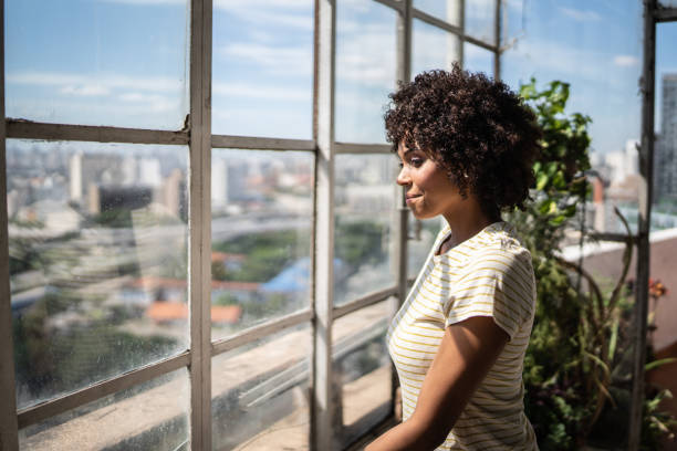 istock Contemplative young woman looking through the window at home 1390883040