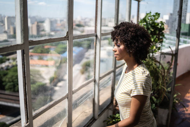 istock Contemplative young woman looking through the window at home 1390883057