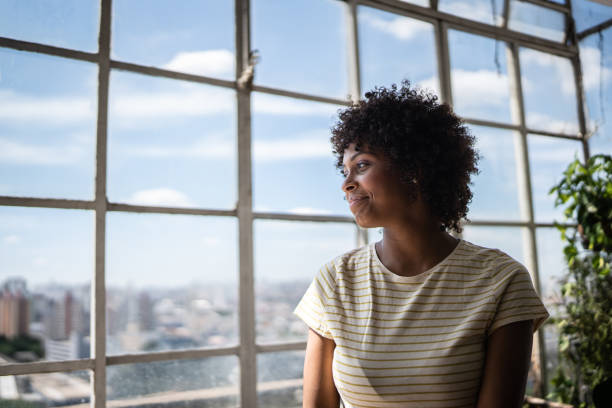 Contemplative young woman looking through the window at home
