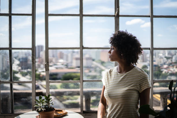 istock Contemplative young woman looking through the window at home 1390883078