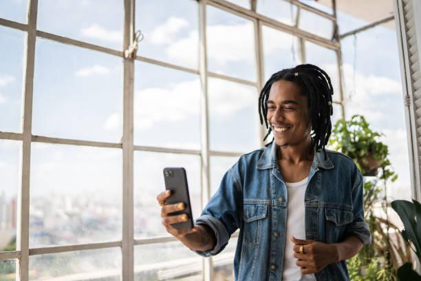 jeune homme en appel vidéo sur le téléphone portable à la maison - photophone photos et images de collection