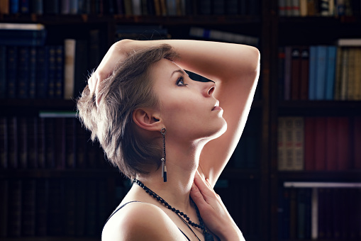 Profile of young beautiful woman, against the bookcase. Selective focus on the eyes