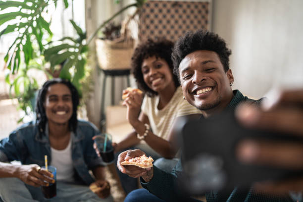 Friends taking selfies or filming while eating pizza at home Friends taking selfies while eating pizza at home black people eating stock pictures, royalty-free photos & images