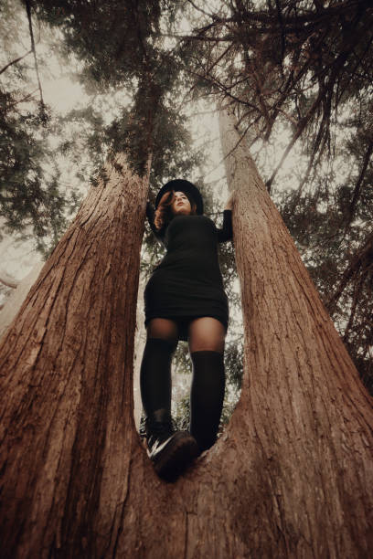 istock Young redhead woman portrait all dressed in black standing on tree trunk 1390884621