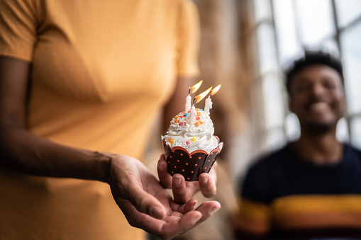 Woman's hand holding a birthday cupcake with candles at home