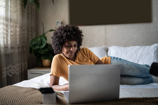 young woman using the laptop on the bed at home - lying down women laptop freedom imagens e fotografias de stock