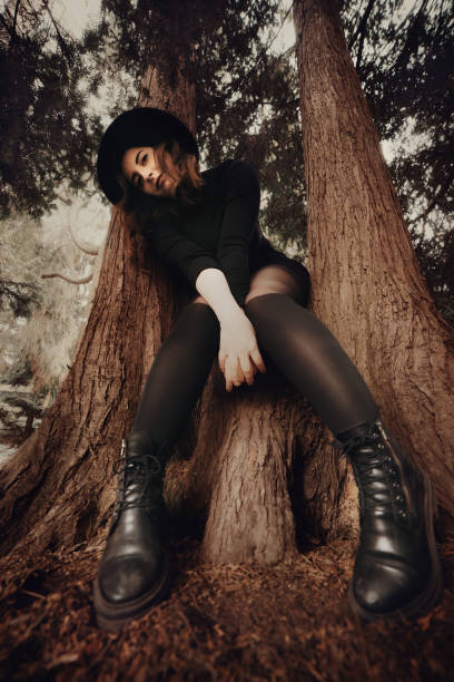 Young woman portrait all dressed in black sitting and posing on tree trunk while looking at camera