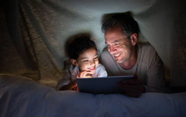 istock Father and daughter reading a book in bed on a tablet computer 1390886904