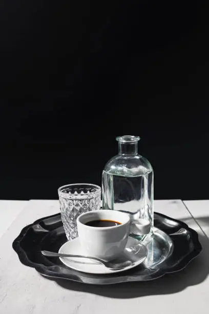 Photo of Black coffee with a glass and pitcher of water on an elegant silver tray with a dark background