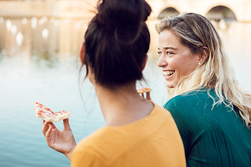 Multiracial best female friends eating italian pizza in urban city street