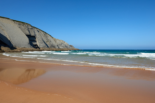 A quiet fine sandy beach with cliffs in the background