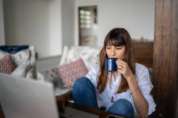 istock Young woman using the laptop and drinking coffee at home 1390895671