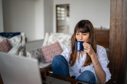 Young woman using the laptop and drinking coffee at home