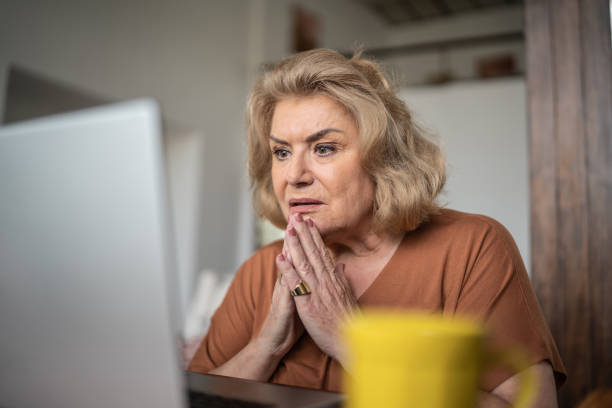 schock ältere frau, die den laptop zu hause benutzt - schlechte nachrichten stock-fotos und bilder