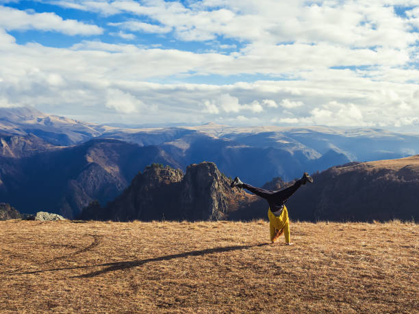 A girl makes a flip on her hands in an autumn meadow lit by the sun, overlooking a mountain valley and a sky in the clouds A girl makes a flip in an autumn meadow lit by the sun, overlooking a mountain valley and a sky in the clouds autumn field tree mountain stock pictures, royalty-free photos & images