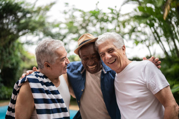 ältere männer umarmen sich auf einer poolparty - active seniors retirement enjoyment swimming pool stock-fotos und bilder