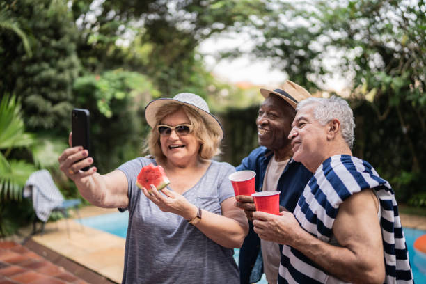 istock Senior friends taking selfies using mobile phone on a pool party 1390900030