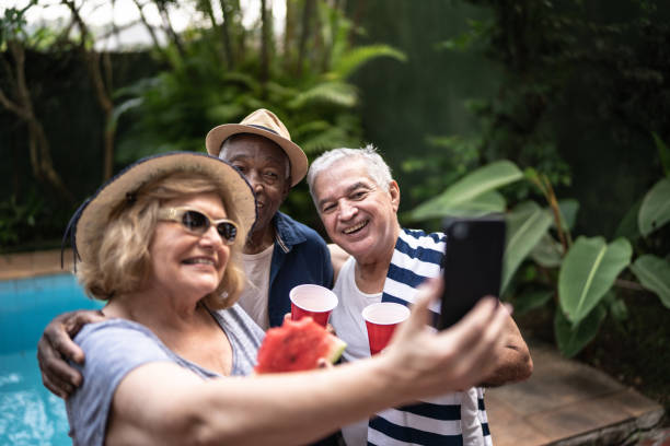 istock Senior friends taking selfies using mobile phone on a pool party 1390900044