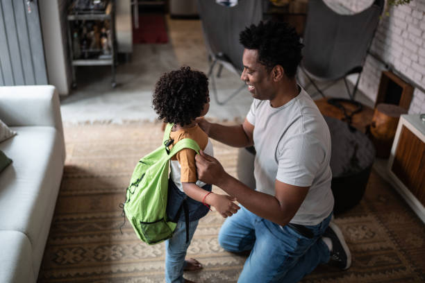 Father helping son with backpack at home before leaving to school