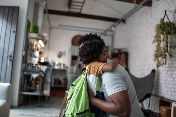 sohn umarmt vater, wenn er von der schule kommt - african descent male education indoors stock-fotos und bilder