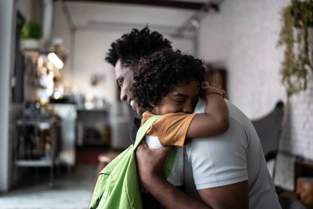 sohn umarmt vater, wenn er von der schule kommt - african descent male education indoors stock-fotos und bilder