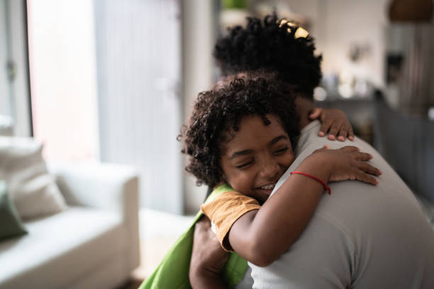 sohn umarmt vater, wenn er von der schule kommt - african descent male education indoors stock-fotos und bilder