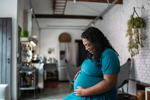 Pregnant woman touching and talking to her belly (baby) at home