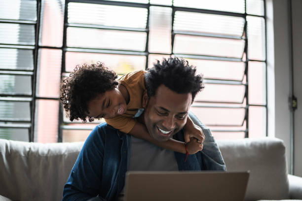 istock Father using the laptop while son is on his back at home 1390901675
