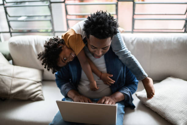 Father using the laptop trying to work while son is on his back at home Father using the laptop trying to work while son is on his back at home child behaving badly stock pictures, royalty-free photos & images
