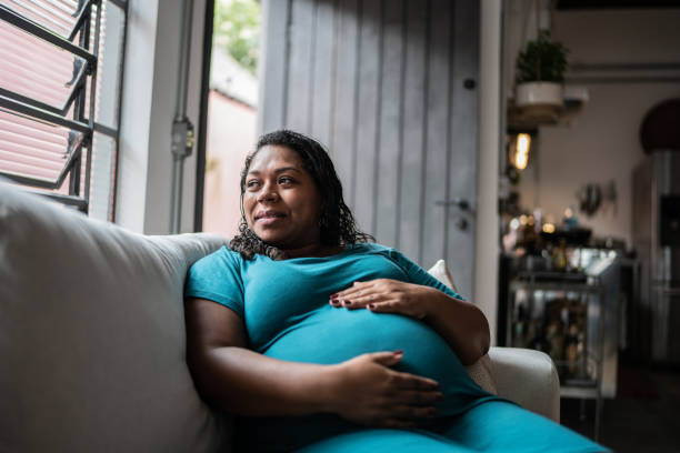 mujer embarazada tocándose el vientre y contemplando en casa - embarazada fotografías e imágenes de stock